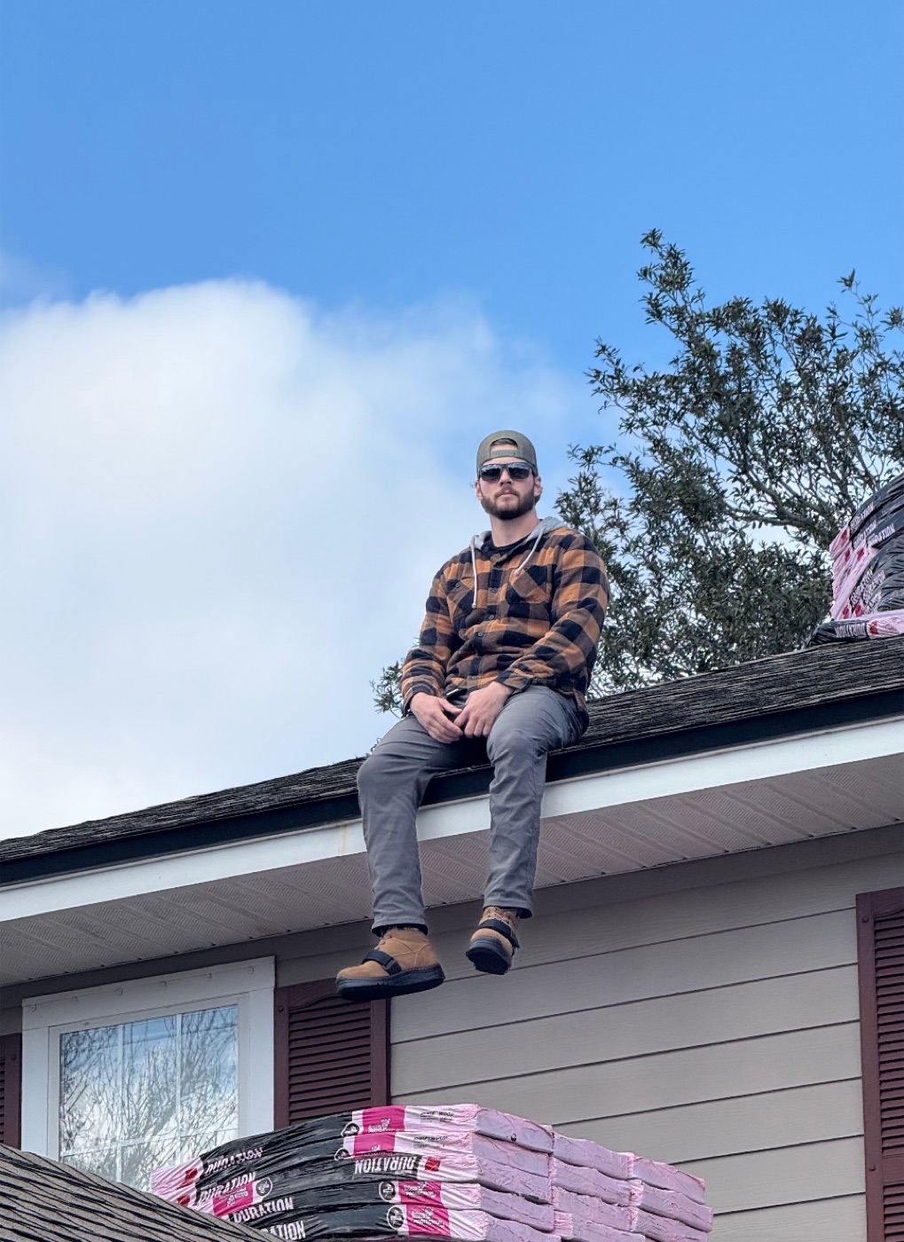 Mark Otterbourg sitting on a roof edge next to fresh shingle bundles on a Jacksonville job